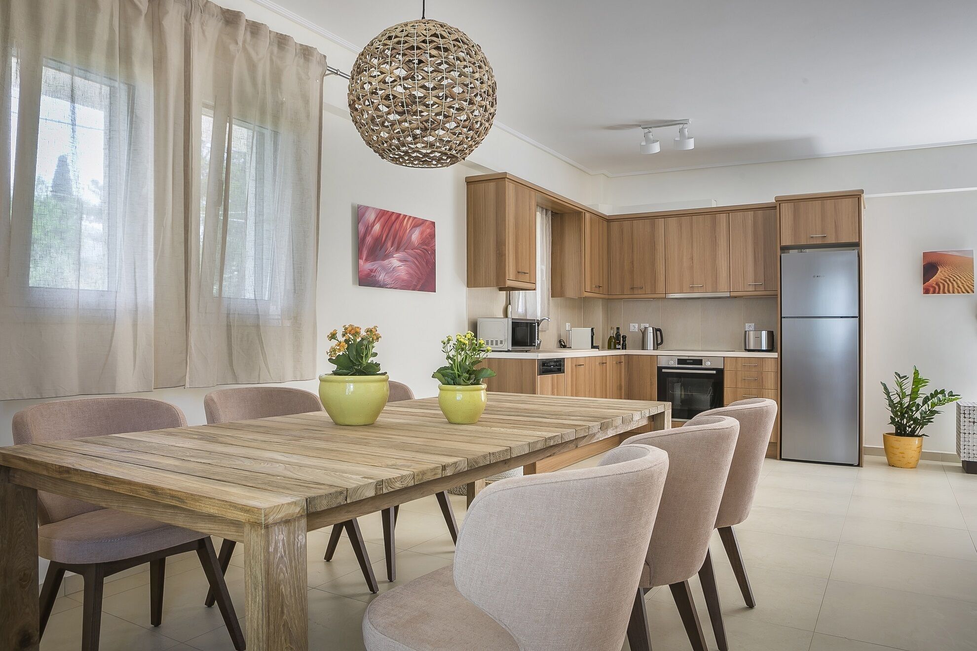 A modern kitchen with wooden cabinets, a stainless steel refrigerator, and a dining area with a wooden table and chairs.