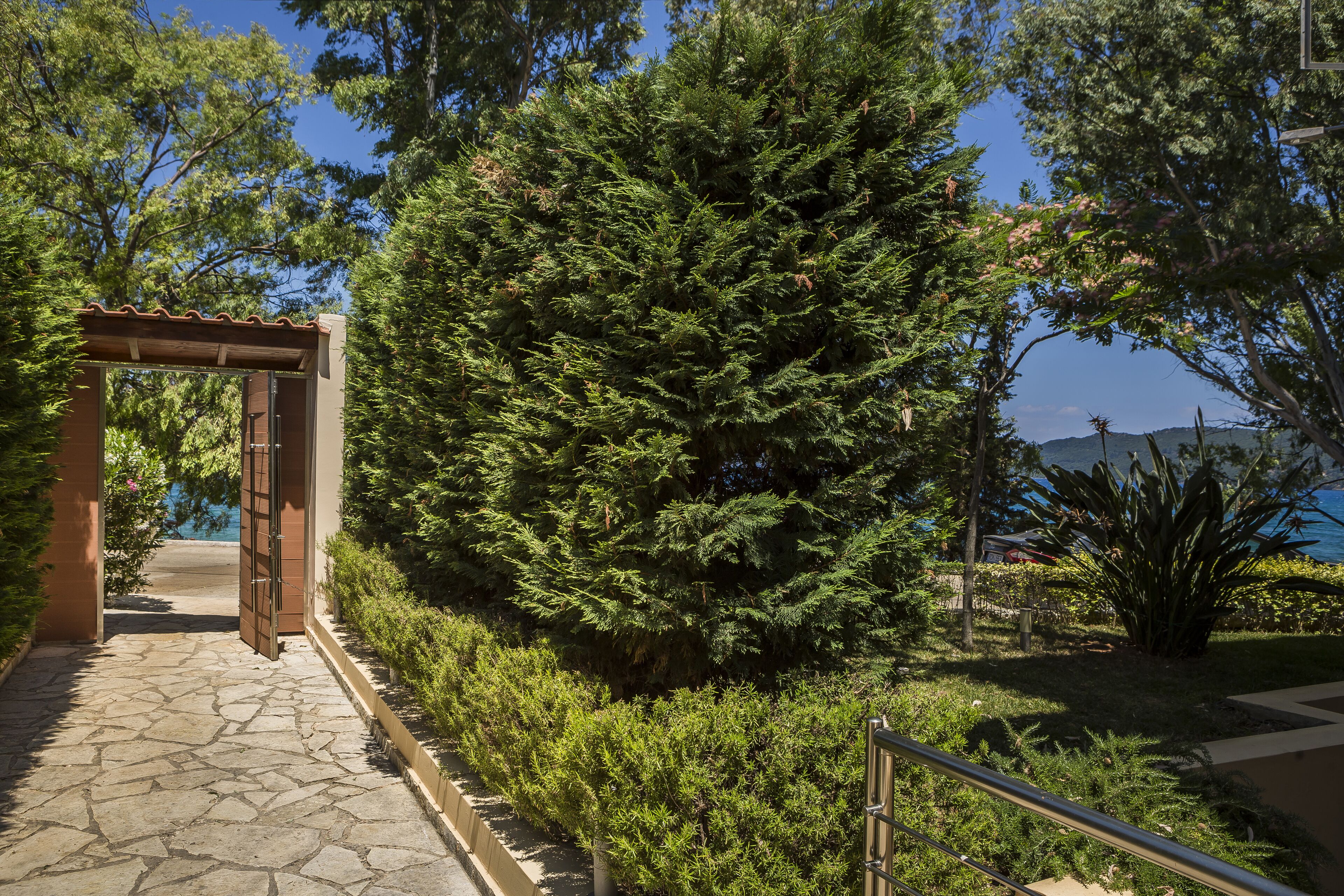 A stone pathway leading to a wooden pergola with a view of a body of water and trees.