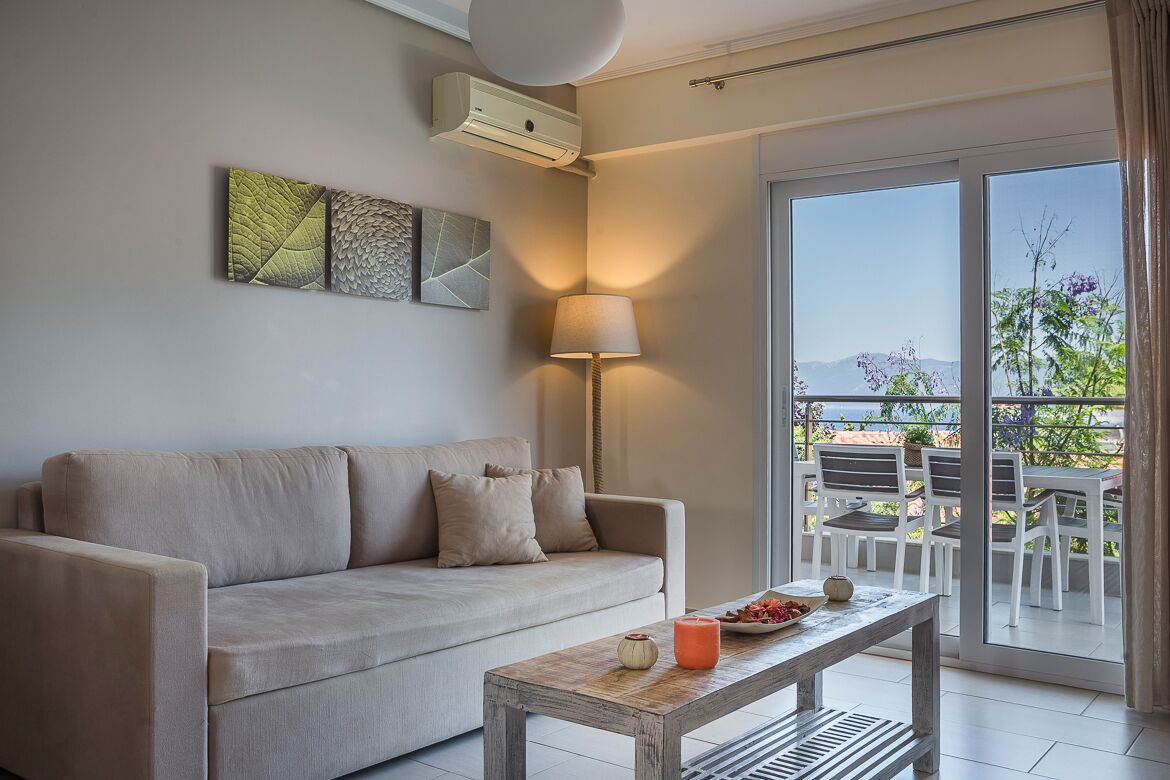 A modern living room with a beige sofa, a wooden coffee table, and a floor lamp. A large window offers a view of the outdoors.