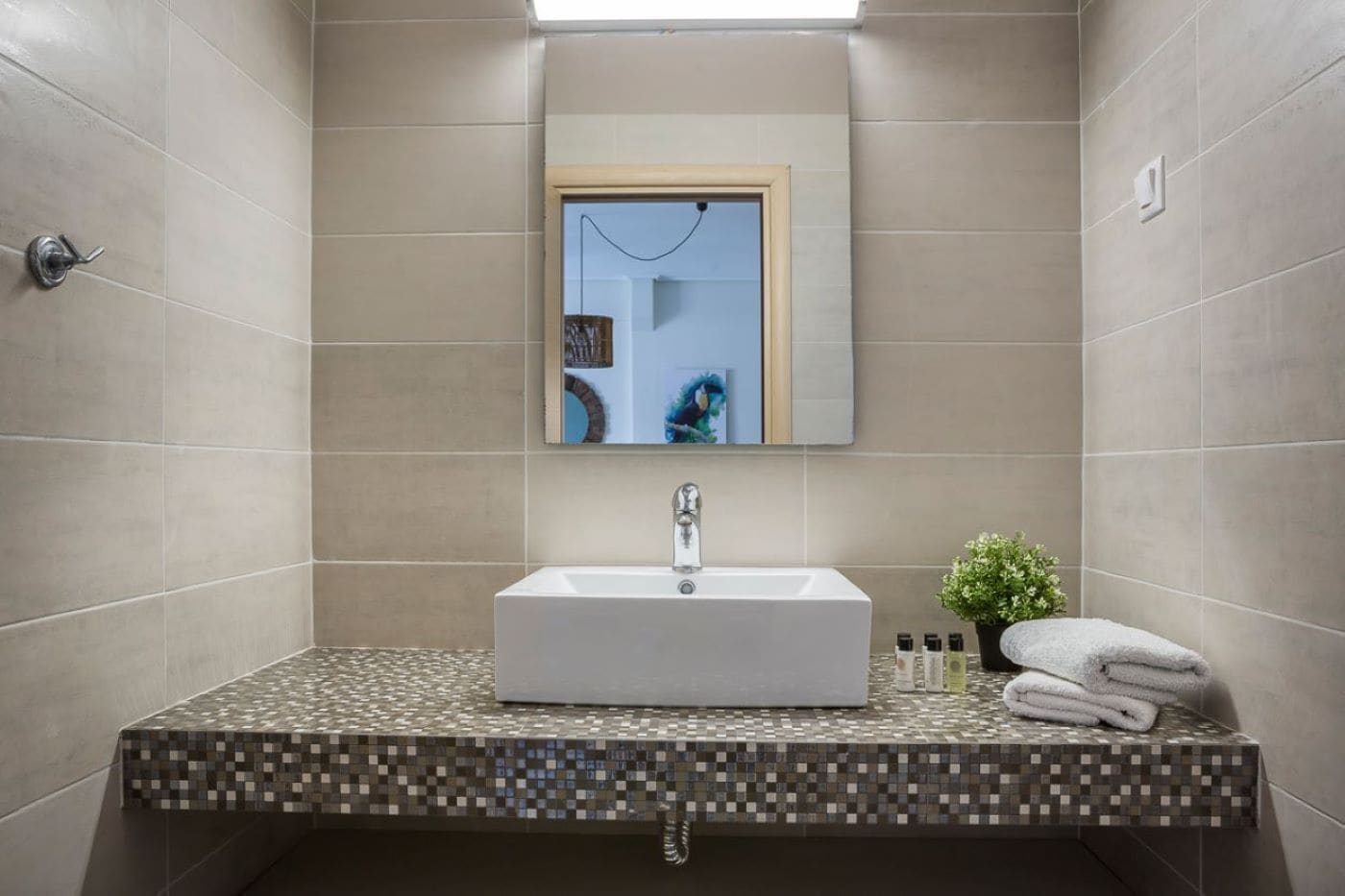 Ein Badezimmer mit gefliesten Wänden, einem Waschbecken mit Spiegel darüber und einer kleinen Pflanze auf der Ablagefläche.