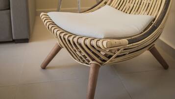 A wicker chair with a cushion, a floor lamp, and a grey sofa in a room with a tiled floor.