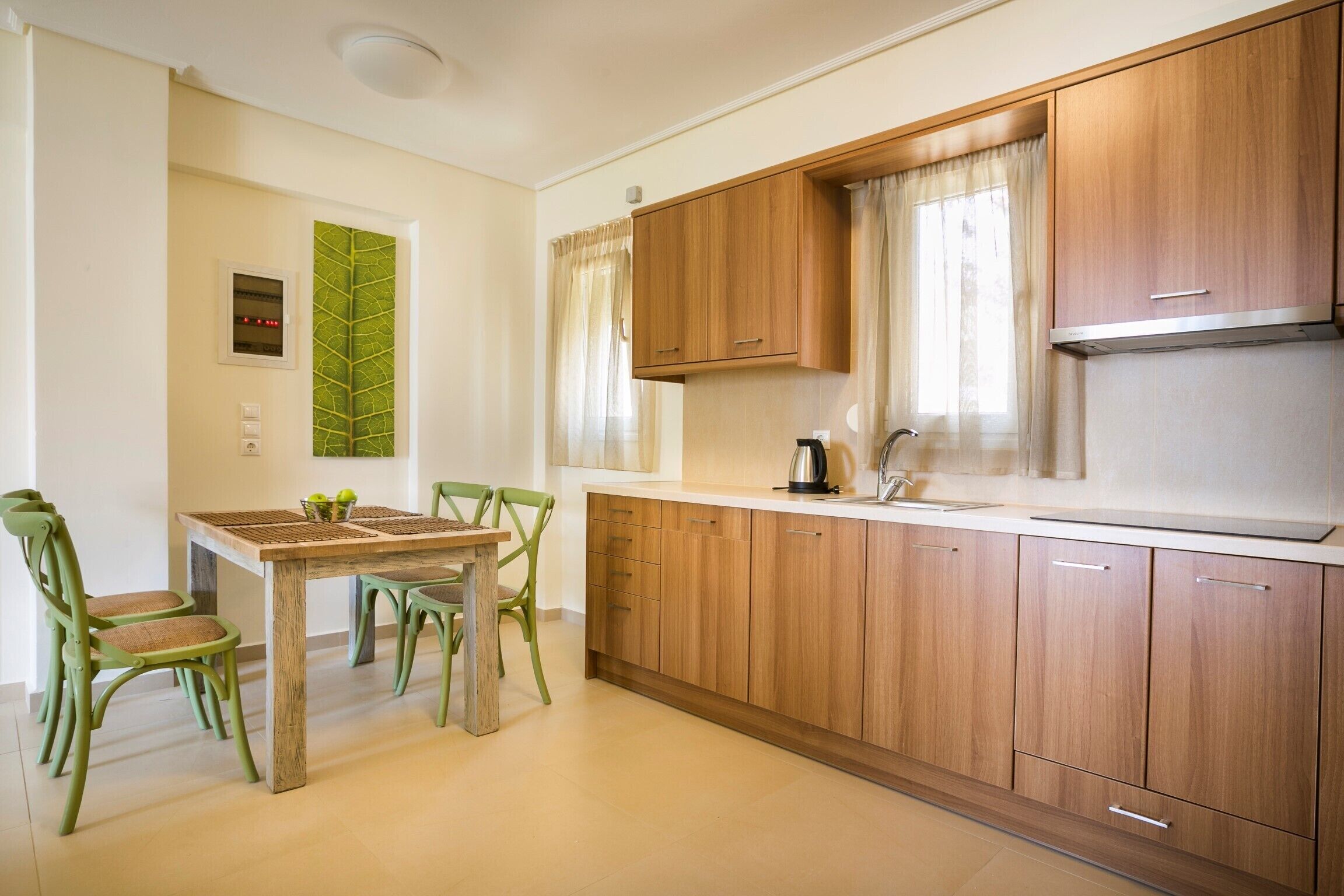A modern kitchen with wooden cabinets, a white countertop, and a dining area with a wooden table and green chairs.