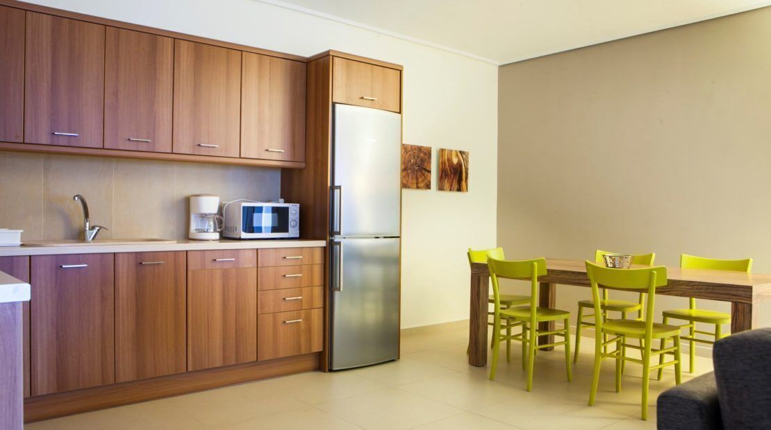 A compact kitchen with wooden cabinets, a stainless steel refrigerator, a microwave, and a coffee maker. There is a dining table with four chairs.