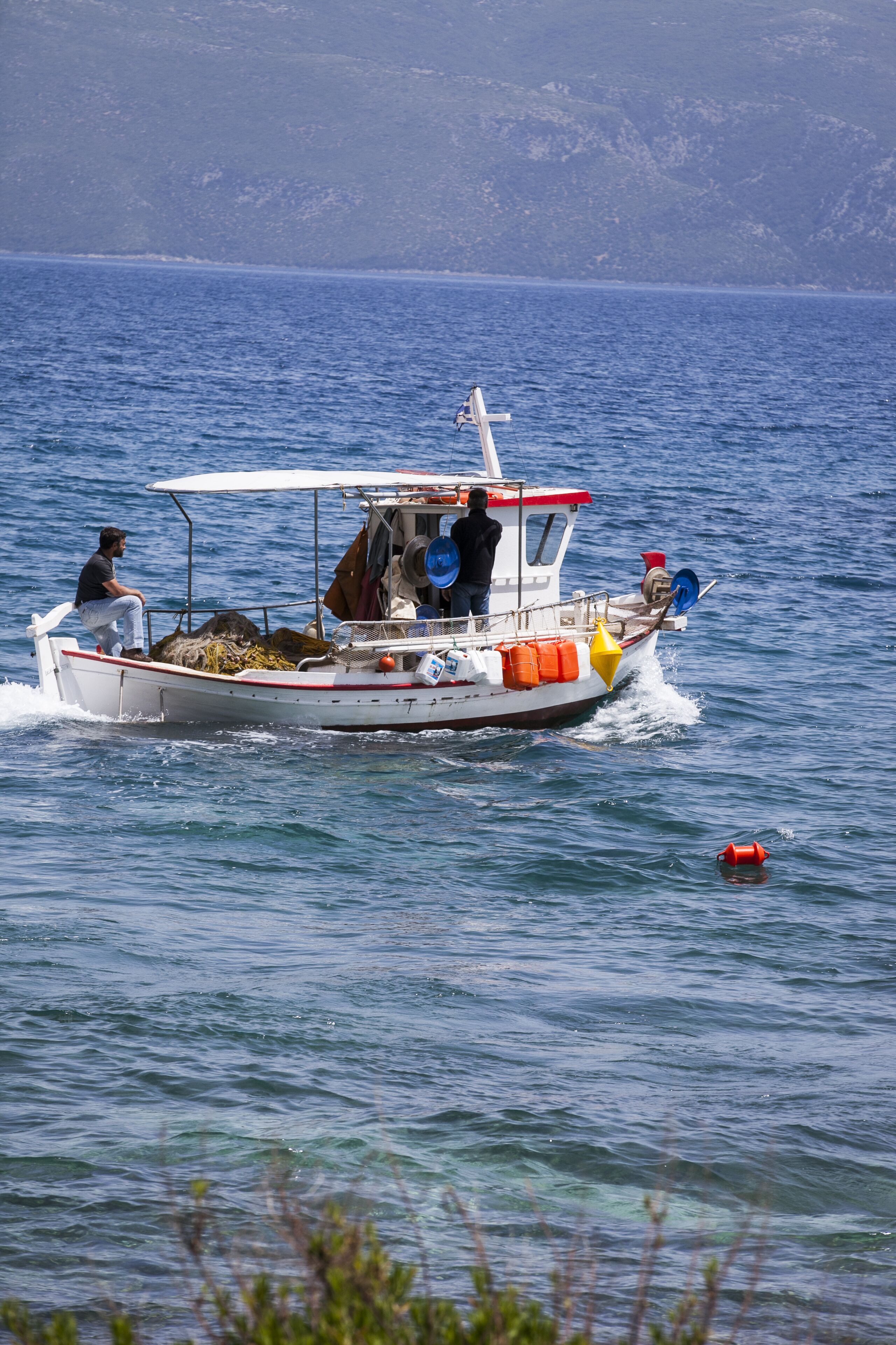 A small boat with a person on board, equipped with various fishing gear and safety equipment.
