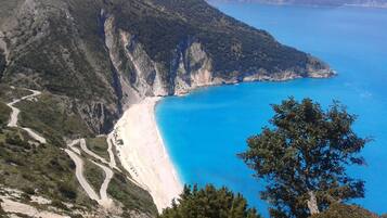 Un paisaje costero con una carretera serpenteante, una playa y un mar azul y transparente.