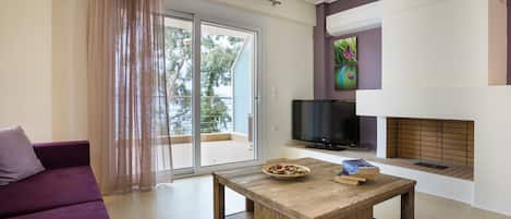Ein modernes Wohnzimmer mit einem violetten Sofa, einem Couchtisch mit Büchern, einem Flachbildfernseher und einem Kamin.