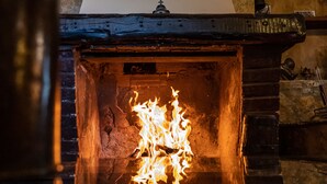Una chimenea de piedra con un reloj encima y un estante de madera a la derecha.