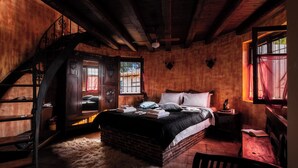 Un dormitorio rústico con cama de ladrillo, vigas de madera, una escalera y una ventana con cortinas.