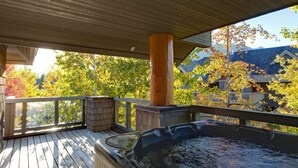 Une terrasse en bois avec un jacuzzi, une colonne en bois et une vue sur les arbres et les maisons aux couleurs automnales.