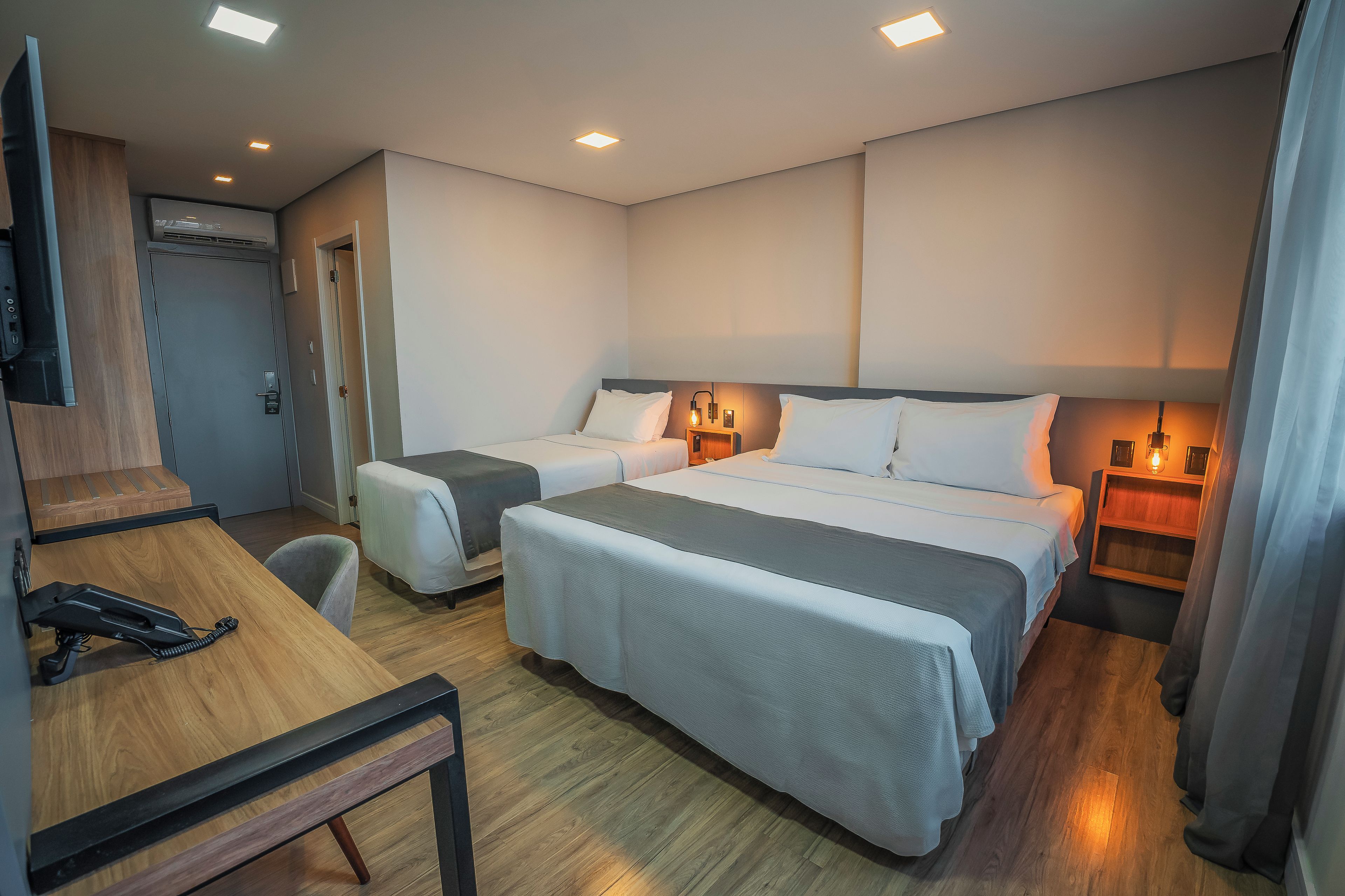 Habitación de hotel con dos camas, un escritorio, una silla, un televisor y una mesita de noche con lámpara.