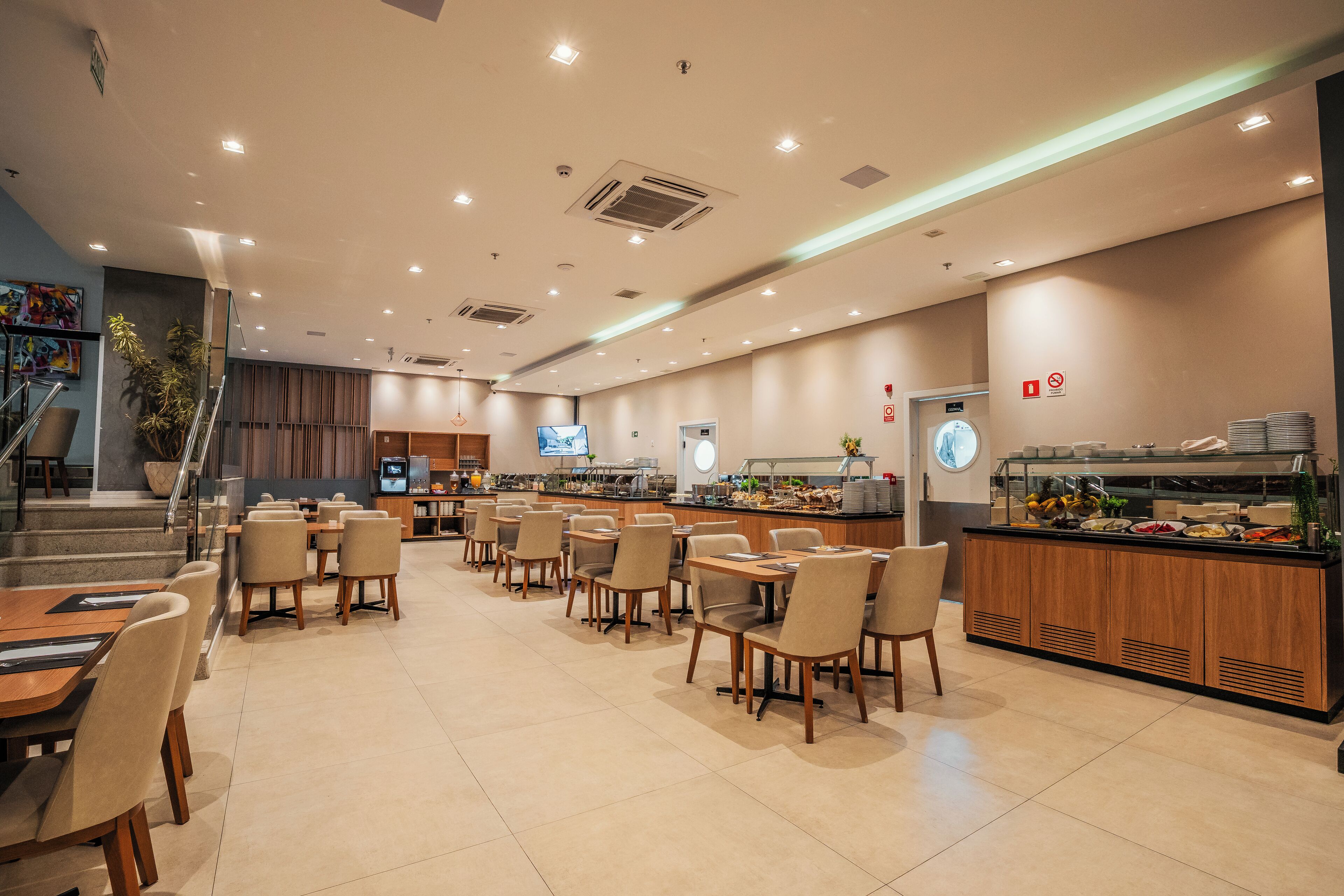Ein modernes Restaurant mit mehreren Tischen, Stühlen, einem Buffet und einer Treppe zu einer oberen Ebene.