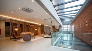Un lobby amplio con techo alto, una escalera de cristal y un área de descanso con mobiliario moderno.
