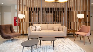 Un vestíbulo moderno con un sofá color crema, dos mesas redondas y un sillón marrón.
