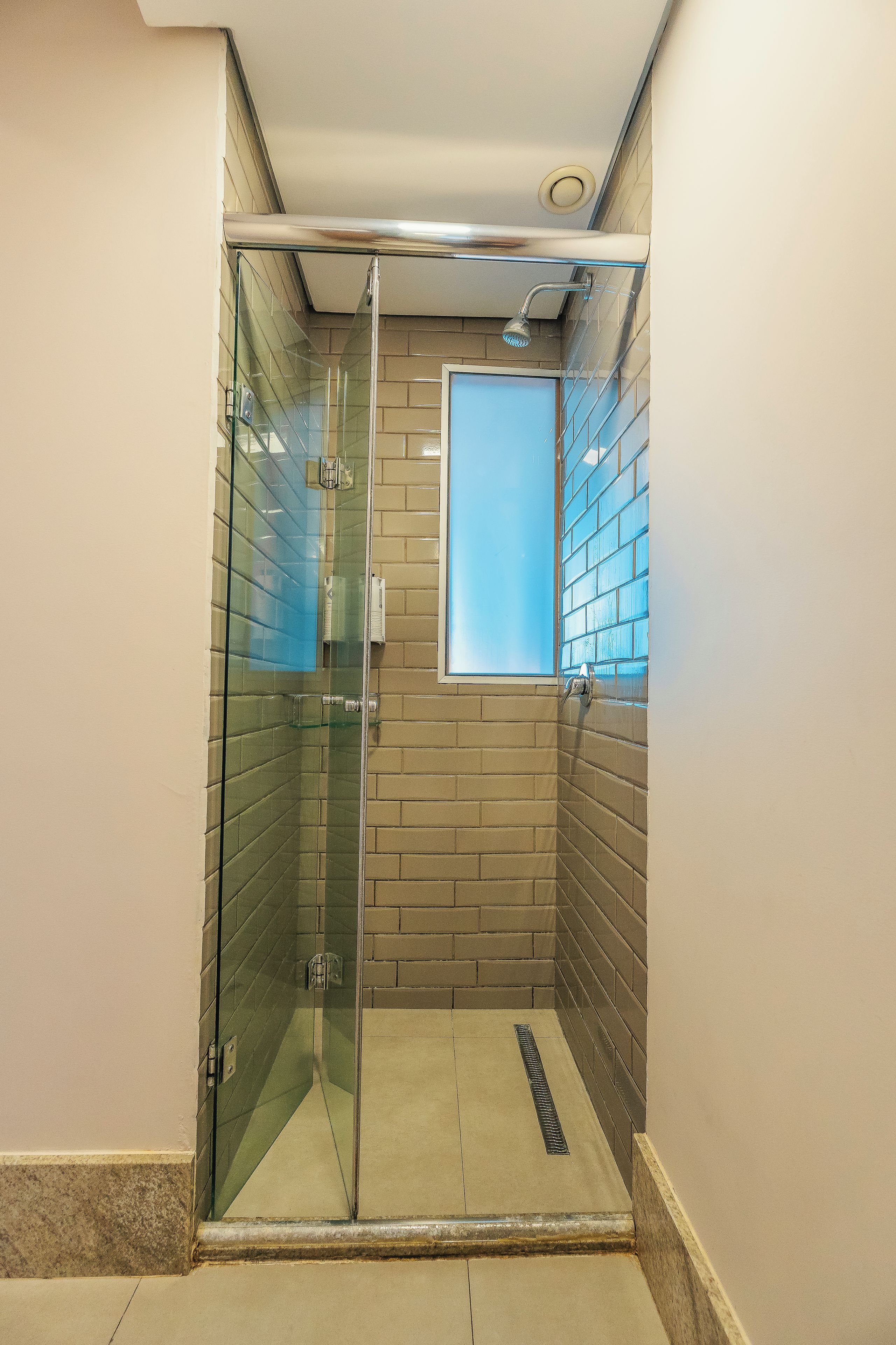 Un box de ducha con mampara de vidrio, paredes de azulejos y desagüe visible.
