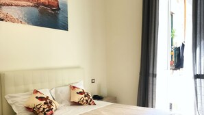 A hotel room with a bed, a nightstand, a painting on the wall, and a view of the outside. - Speranzella 86 (Naples)