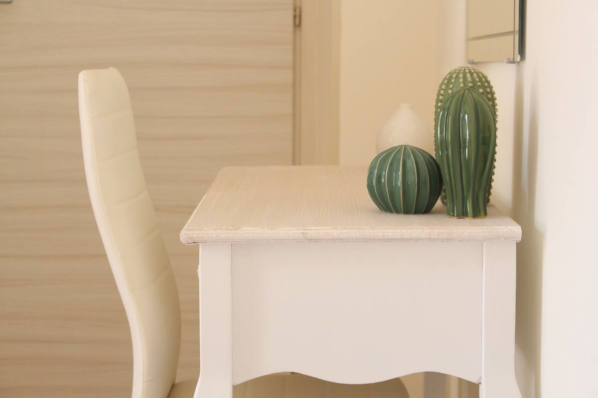 Una silla blanca y una mesita con dos jarrones verdes.