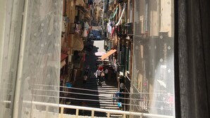A narrow street with buildings on both sides, balconies with hanging laundry, and a clear blue sky. - Speranzella 86 (Naples)