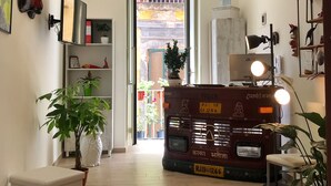 A hallway with a white bench, a potted plant, a shelf with books and decorative items, and a vintage vehicle with lights. - Speranzella 86 (Naples)