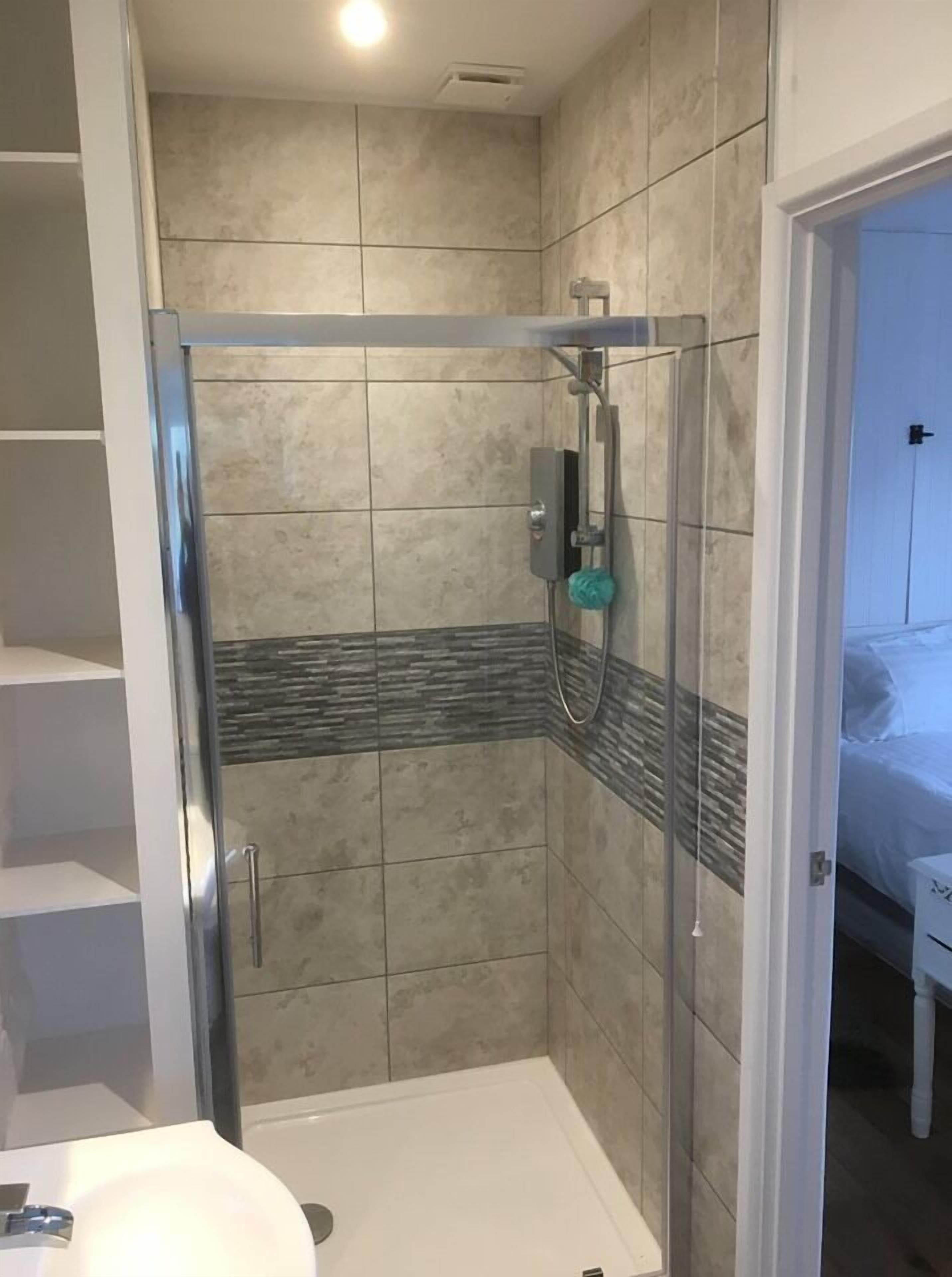 Ein modernes Badezimmer mit einer Duschkabine aus Glas, gefliesten Wänden und einem weißen Waschbecken.