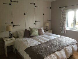 Un dormitorio con una cama grande, dos mesitas de noche con lámparas, una ventana con cortinas florales y una pared decorada con soportes ornamentales.