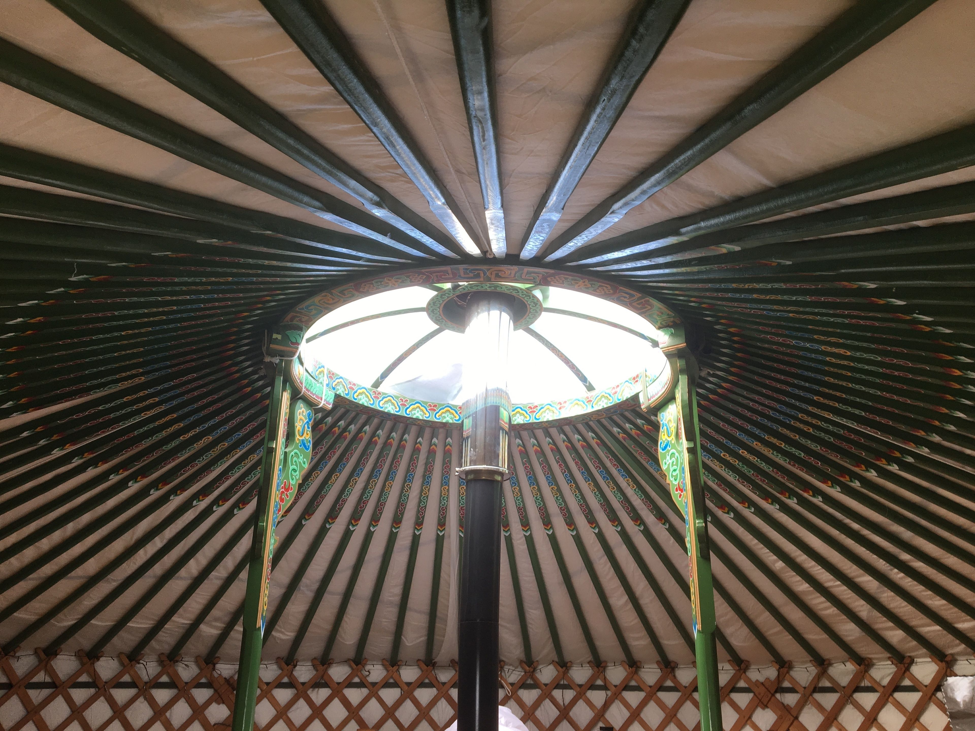 A yurt with a circular skylight and colorful patterns on the wooden beams.