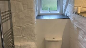 A small bathroom with a stone wall, a window, a toilet, and a metal towel rack.