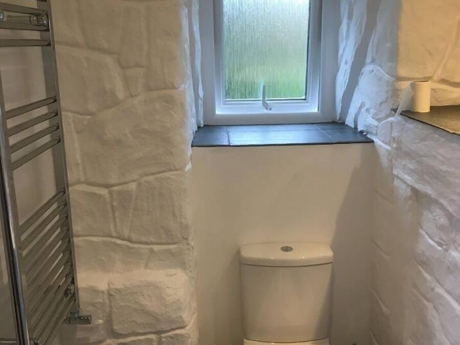 A small bathroom with a stone wall, a window, a toilet, and a metal towel rack.