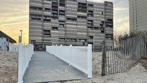 A multi-story residential building with a balcony on each floor, a wooden walkway leading to the entrance, and a sandy beach area. - Beach Front with Amazing Views from Oceanside & Bayside (Ocean City)