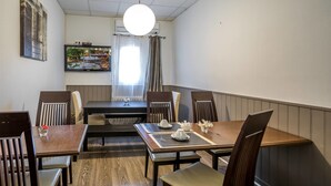 A dining area with a table set for four, chairs, a television mounted on the wall, and a window with curtains. - Hôtel Des Moulins (Allauch)