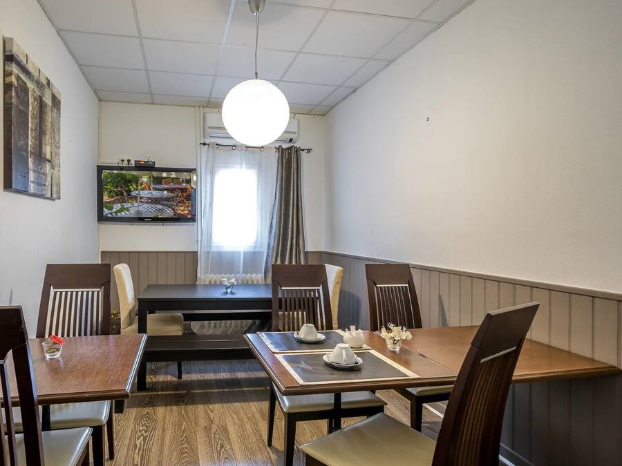 En matplats med ett bord för fyra personer, stolar, en tv som är monterad på väggen och ett fönster med gardiner.