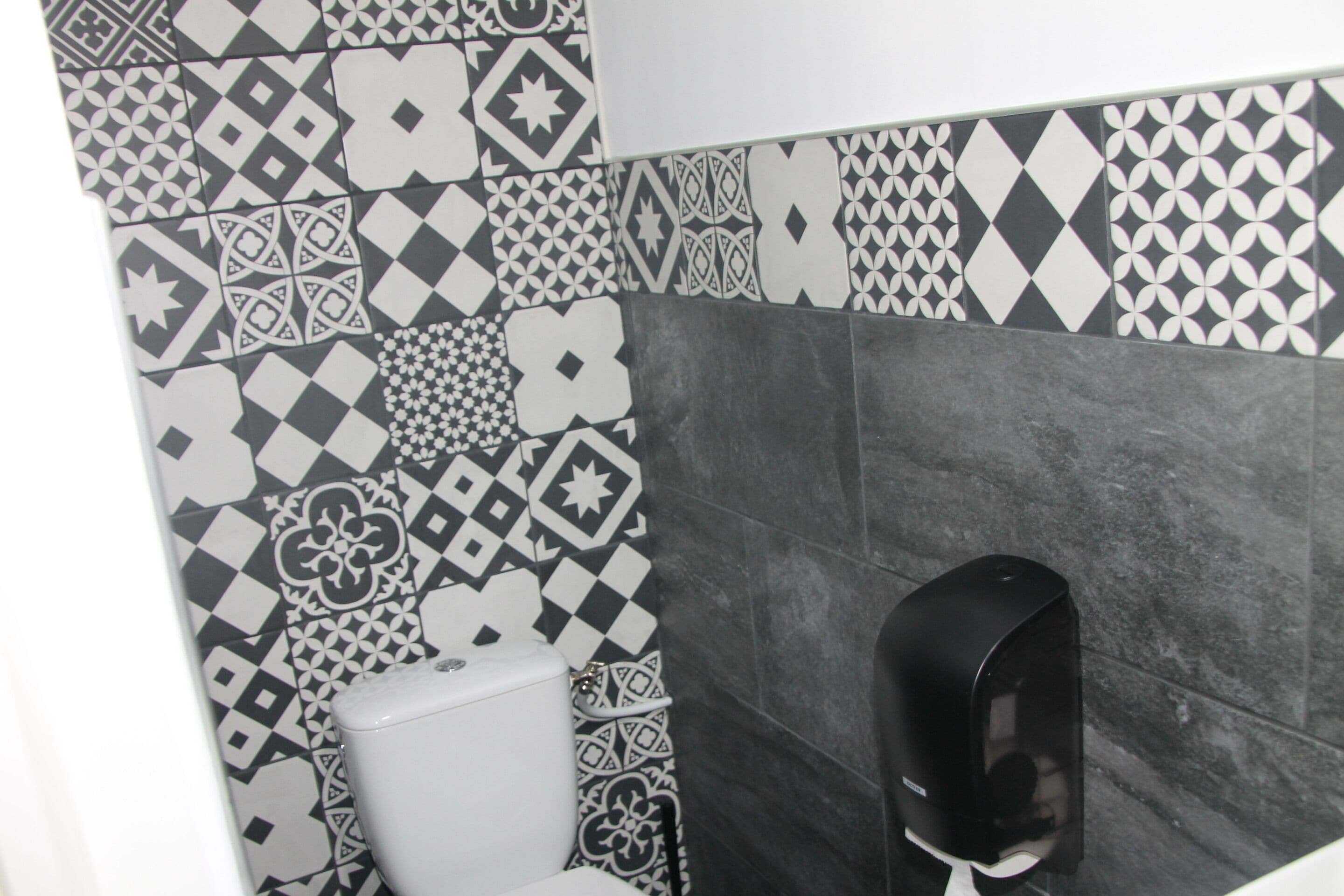 Un baño con azulejos estampados y un dispensador de jabón.