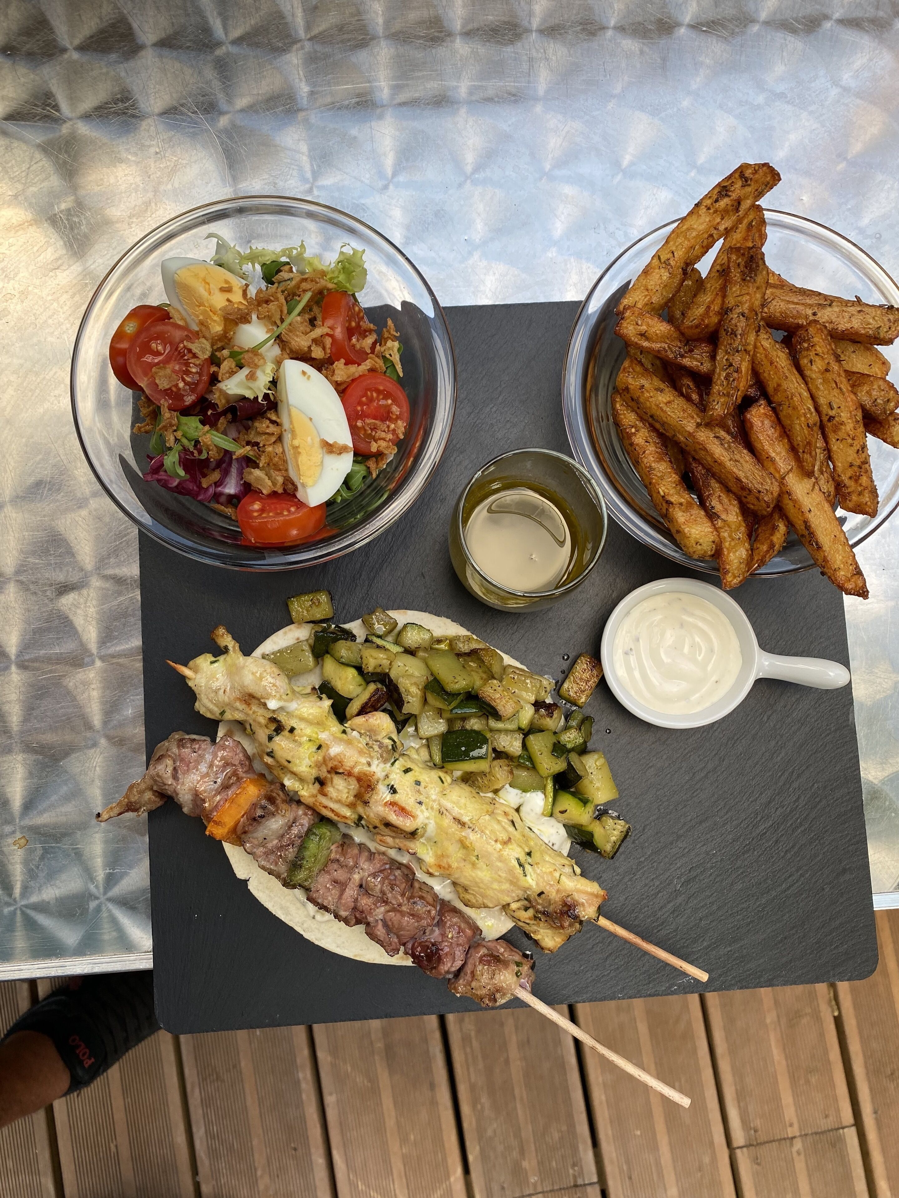 Un plateau repas contenant une salade, des frites et de la viande grillée, posé sur une table.