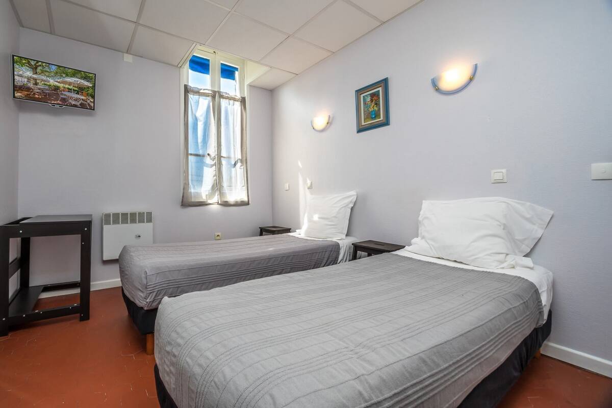 Een hotelkamer met twee bedden, een televisie, een raam met gordijnen en een klein tafeltje.