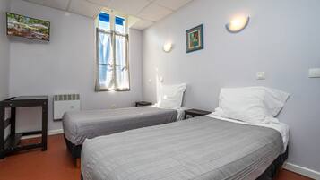 Una habitación con dos camas, televisión, ventana con cortinas y una lámpara de pared.