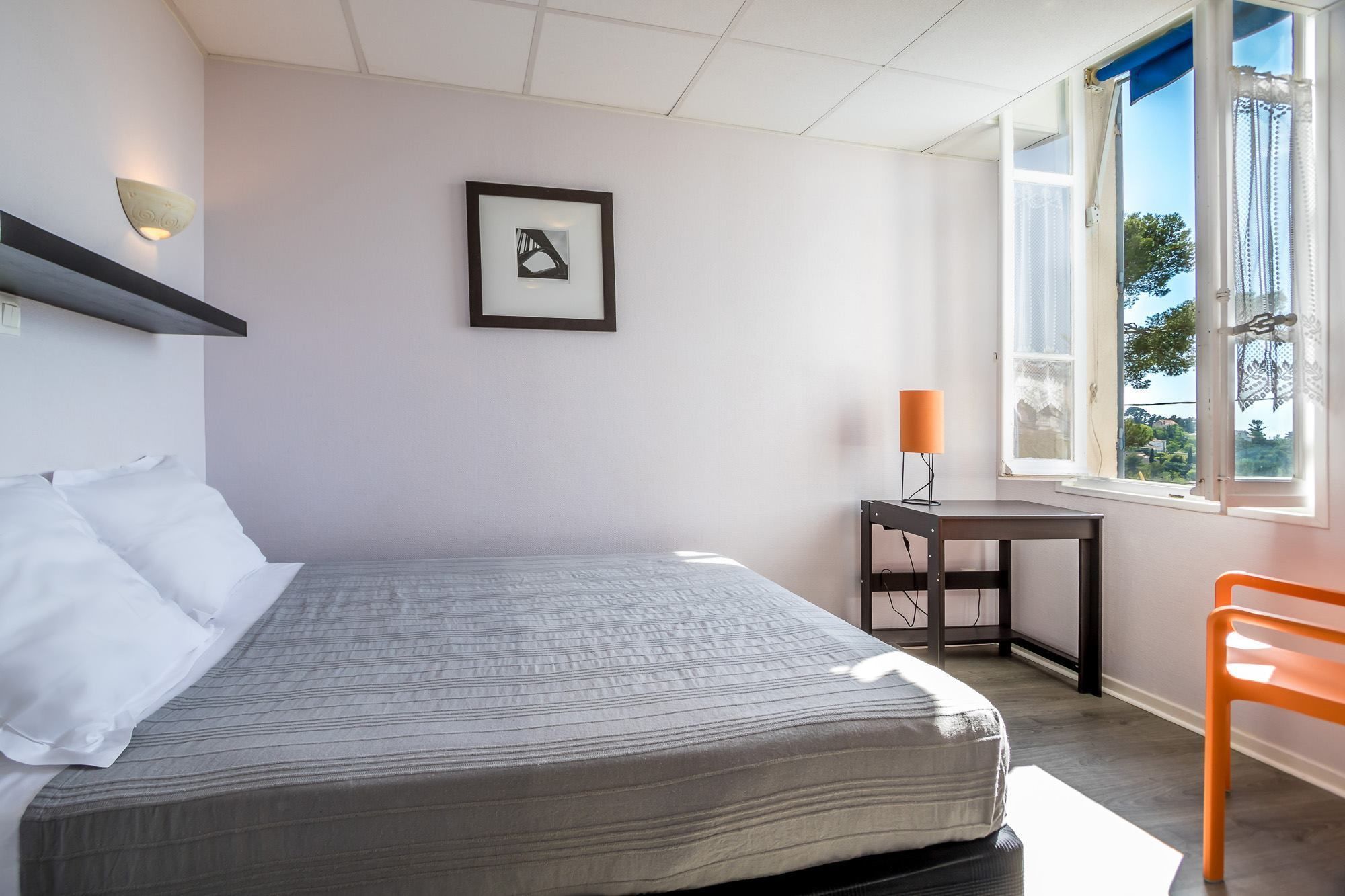 Een slaapkamer met een bed, een bureau, een stoel, een raam en een wandlamp.