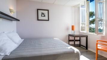 Een slaapkamer met een bed, een bureau, een stoel, een raam en een wandlamp.