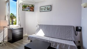 A bedroom with a bed, bedside table, desk, chair, and a phone on the wall. - Hôtel Des Moulins (Allauch)
