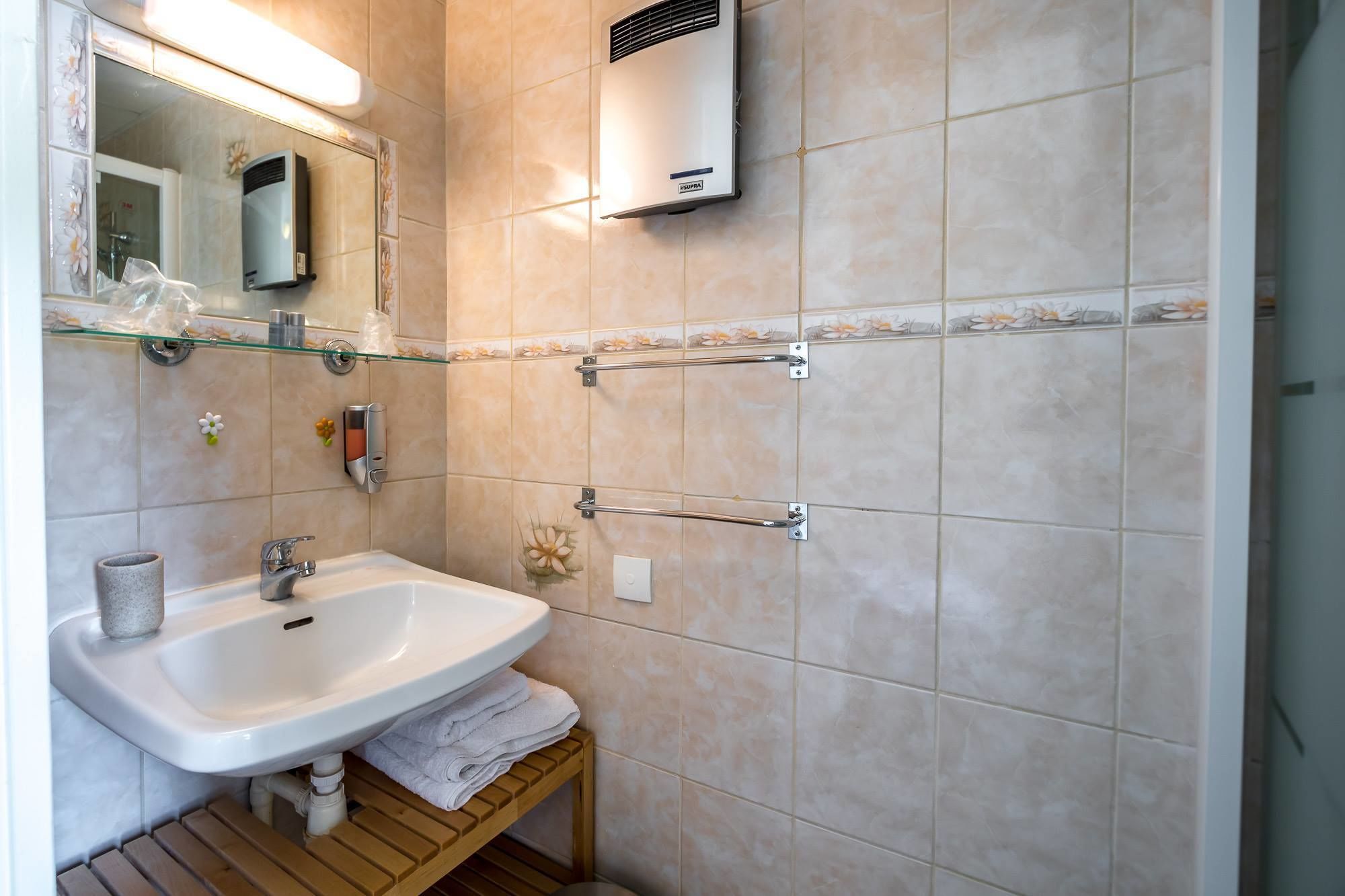 Un baño moderno con un lavamanos blanco, un estante de vidrio con artículos de aseo, un perchero y un aire acondicionado instalado en la pared.