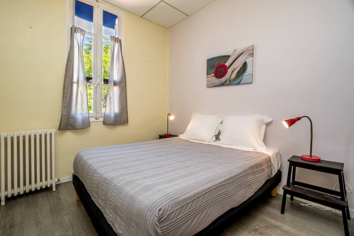 Een slaapkamer met een bed, twee nachtkastjes, een radiator en een raam met gordijnen.