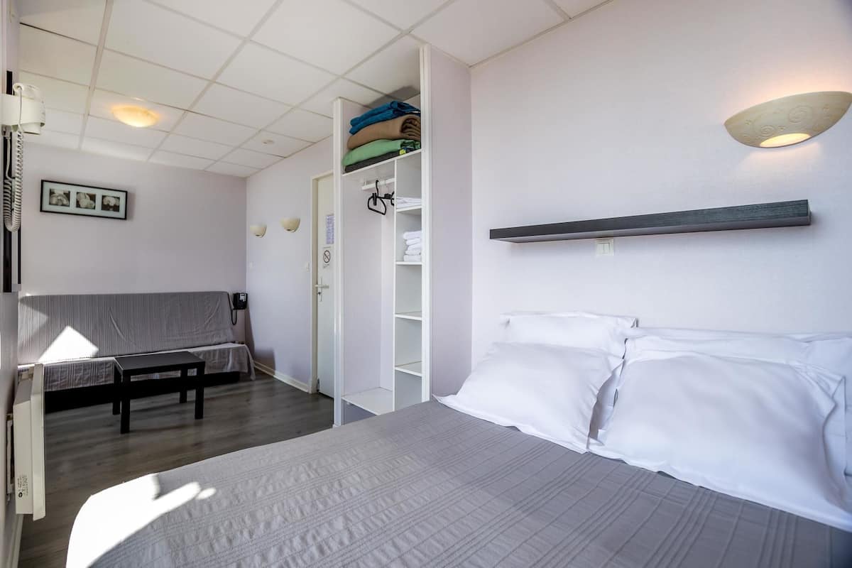 Een hotelkamer met een bed, bureau, stoel, kledingkast en nachtkastje.