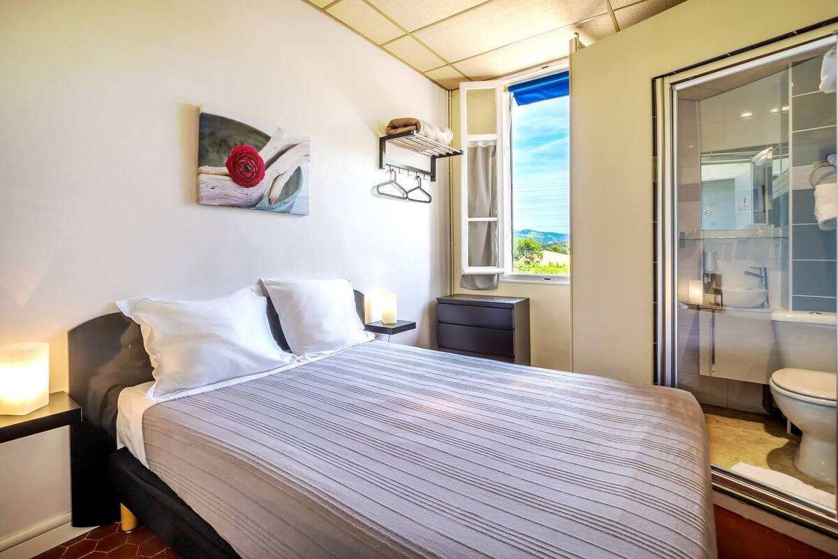 Een moderne slaapkamer met een bed, nachtlampjes, een raam met uitzicht en een badkamer met een douchecabine van glas.