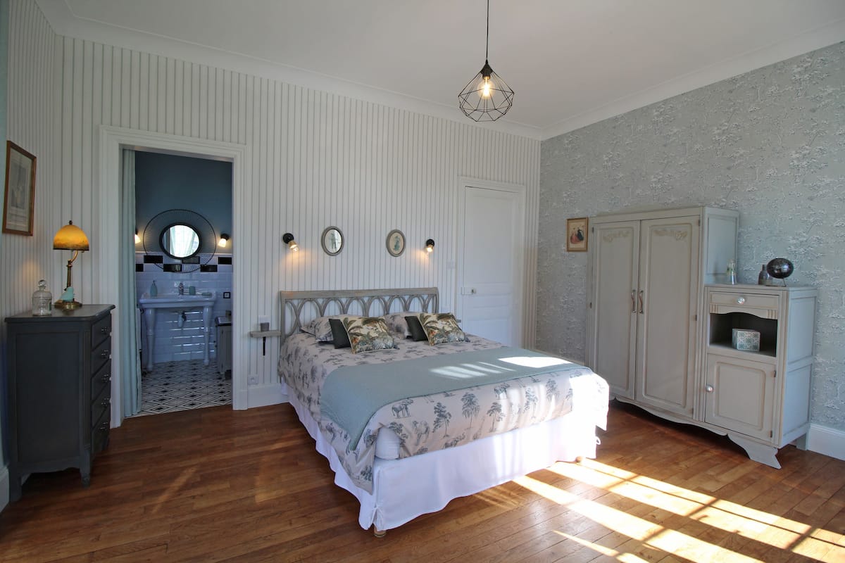 Un dormitorio con cama, cómoda y un baño pequeño visible a través de una puerta abierta.