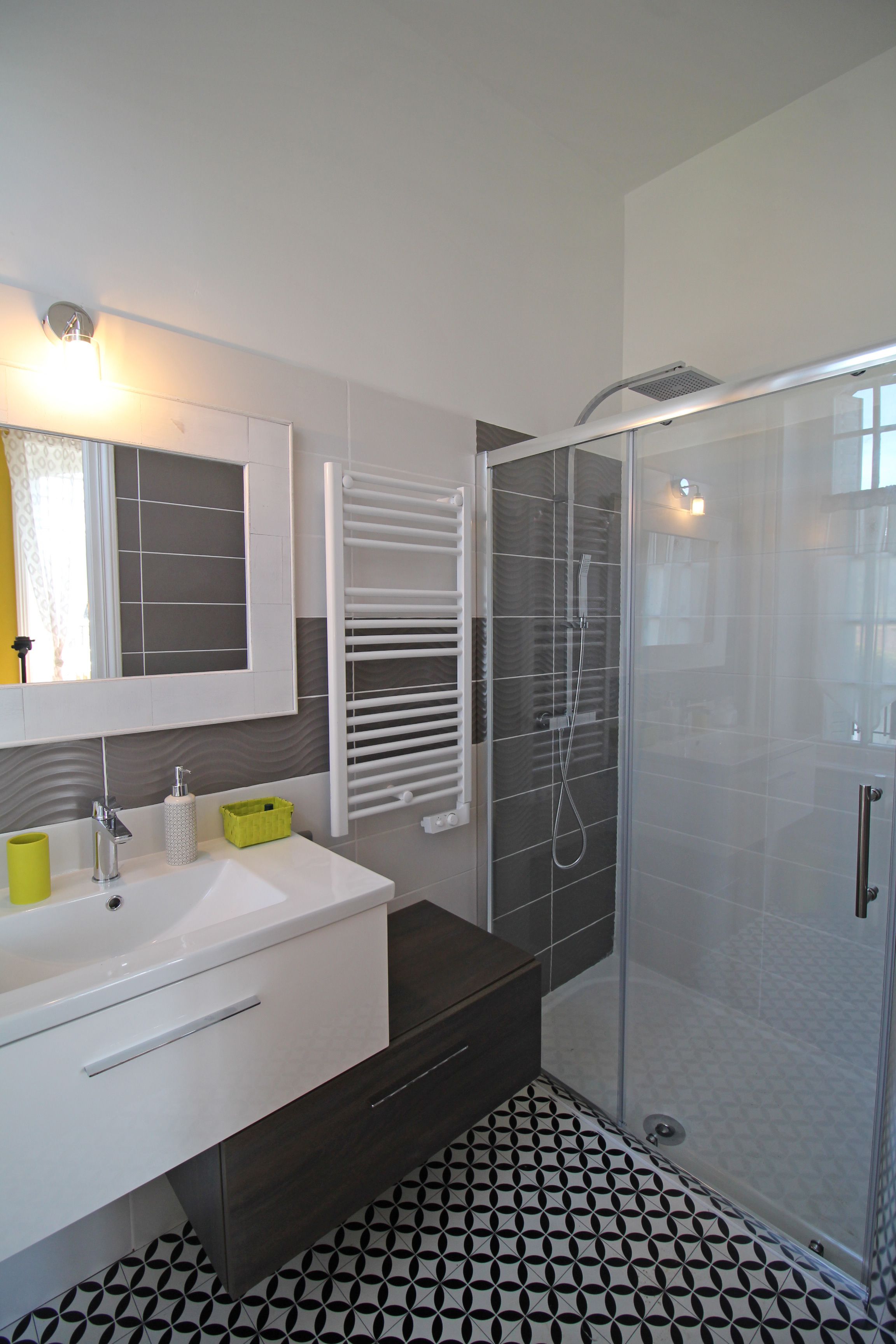 Une salle de bain moderne avec un lavabo blanc, un miroir et une cabine de douche en verre.