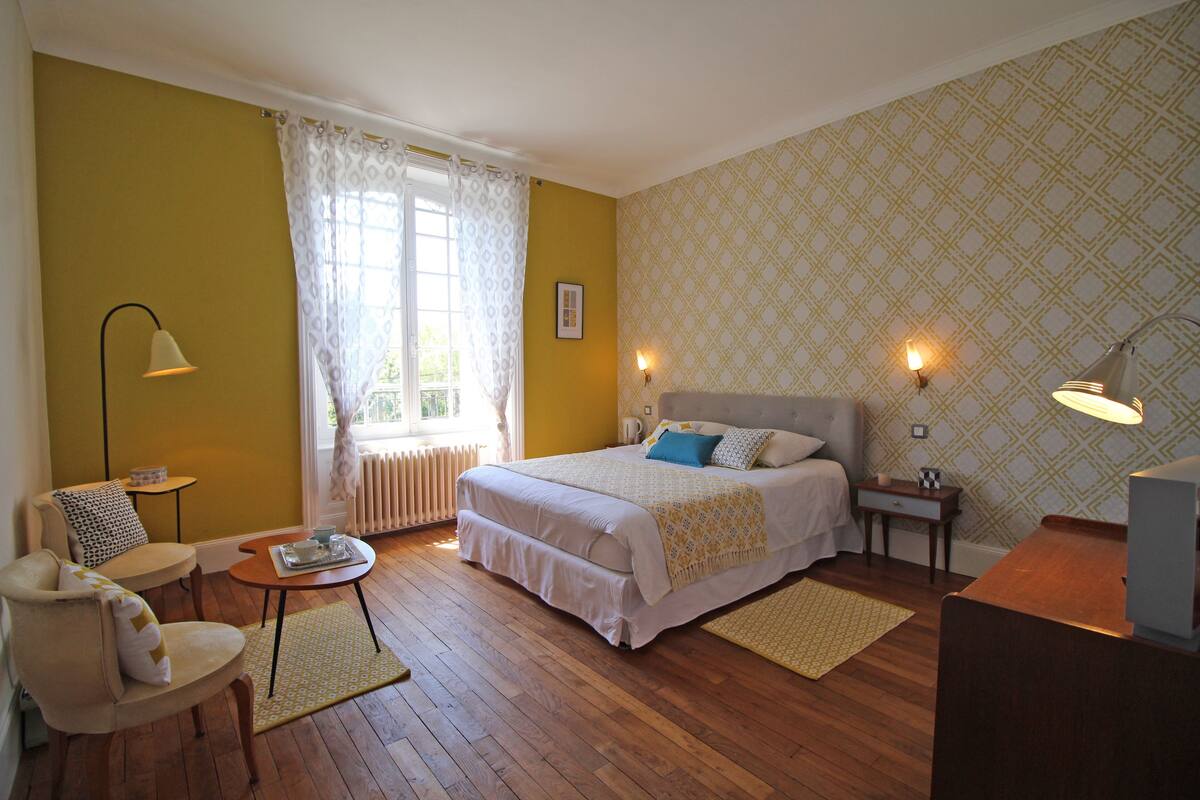 Un dormitorio con una cama, una silla, una mesa y una lámpara.