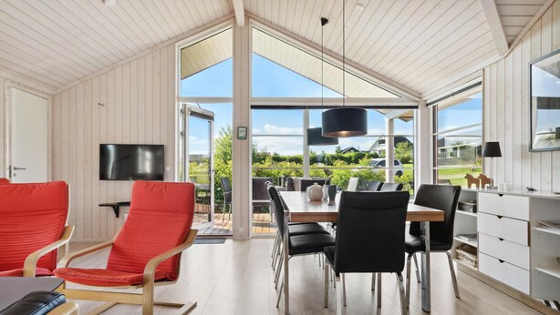 A spacious room with a large dining table, multiple chairs, a TV, and a view of greenery outside.