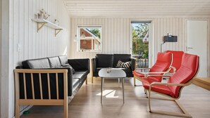 A modern living room with a wooden floor, a black leather sofa, a red leather armchair, and a small white table.