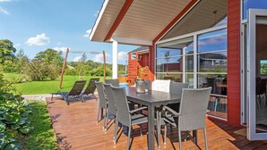 An outdoor deck with a table and chairs, a swing set, and a view of a green landscape.