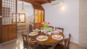 Un comedor con una mesa de madera redonda dispuesta para cuatro personas, rodeada de sillas de madera. En el centro, un jarrón con flores.