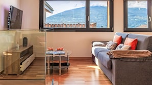Un salon moderne avec un canapé, une table basse en verre, un téléviseur et une vue sur les montagnes grâce à de grandes fenêtres.