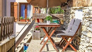 Une table en bois avec un banc, un parasol et des plantes en pot, le tout installé sur une terrasse dotée d’un mur en pierre et d’une clôture en bois.